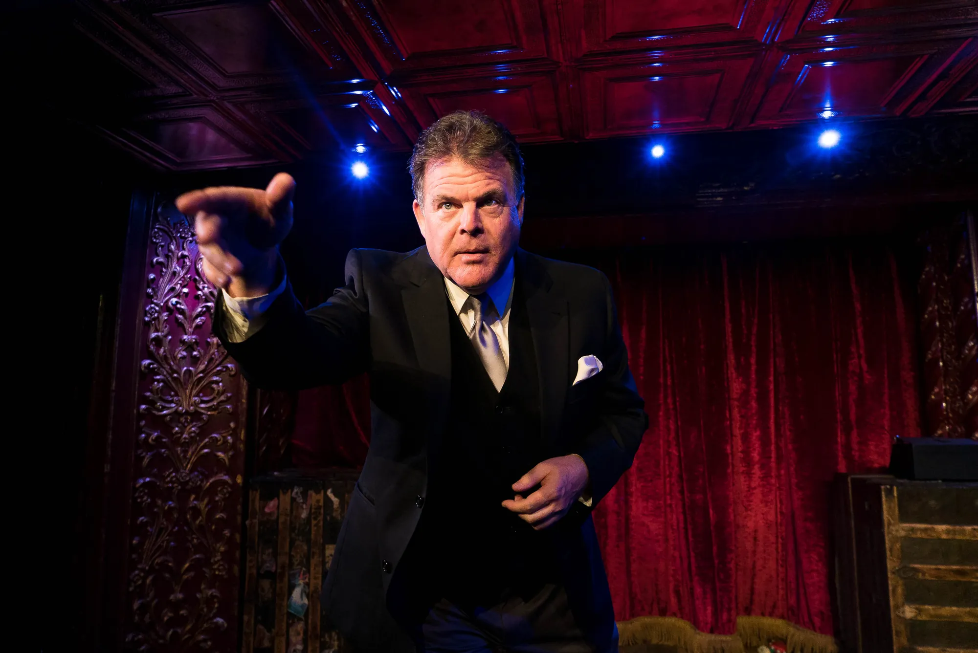 John Carney with a hat in front of red theater curtains
